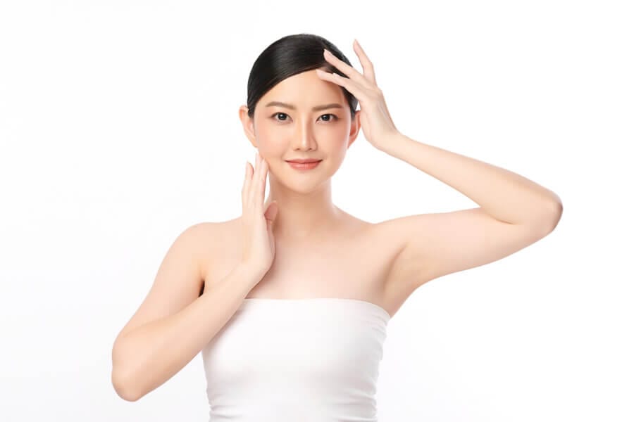 Asian woman receiving a professional facial treatment while relaxing under soft spa lighting.